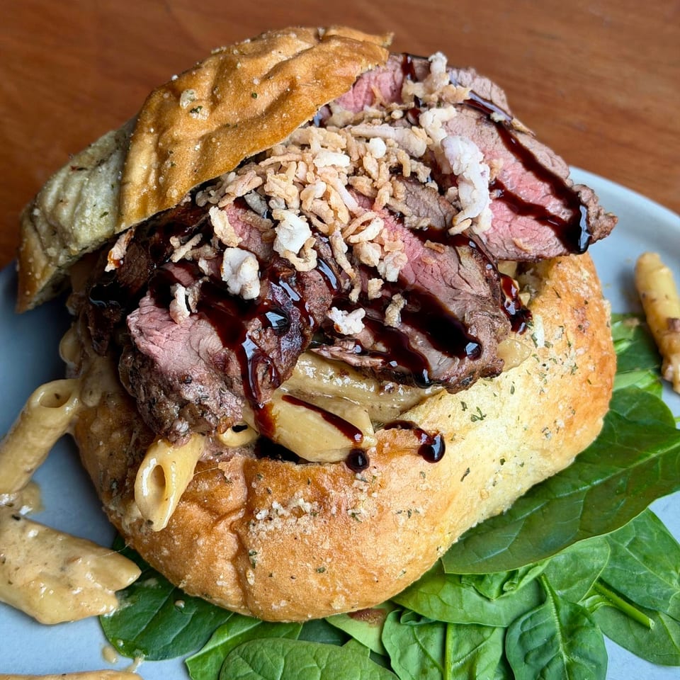 Savory bread bowl filled with steak, macaroni and cheese, crispy onions, and balsamic glaze.
