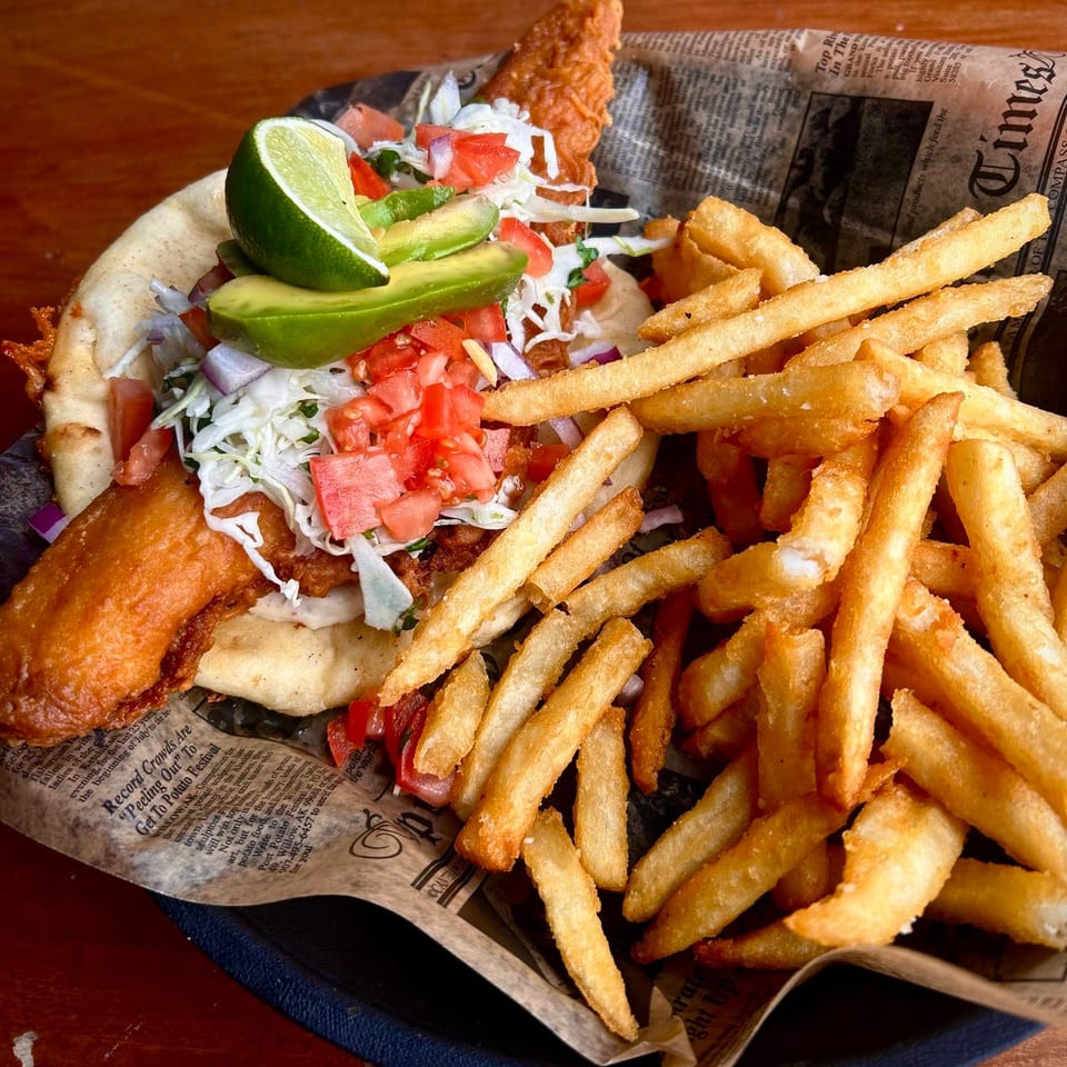 Crispy fish taco with avocado, lime, and salsa, served with a side of golden french fries.