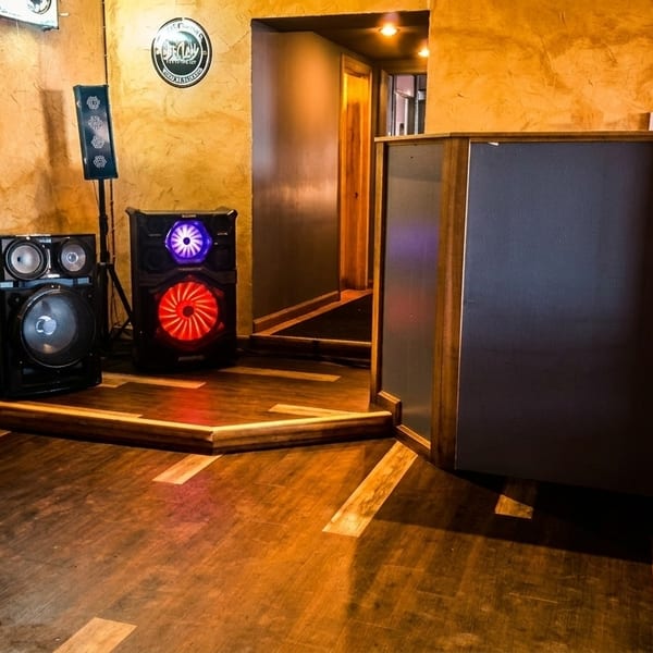 A dimly lit restaurant interior with speakers, a DJ booth, and wooden floors.