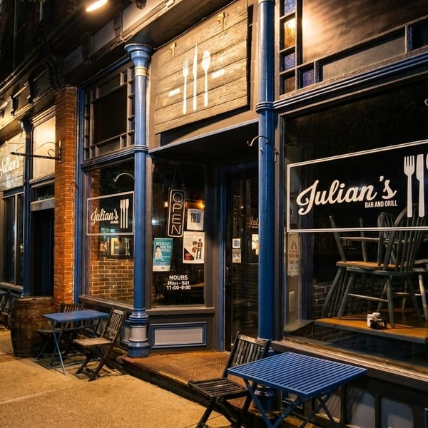 Julian's Bar and Grill exterior at night, with blue tables and chairs on the sidewalk.
