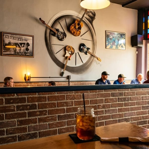 Restaurant interior with brick walls, patrons, and guitars arranged like a clock on the wall.