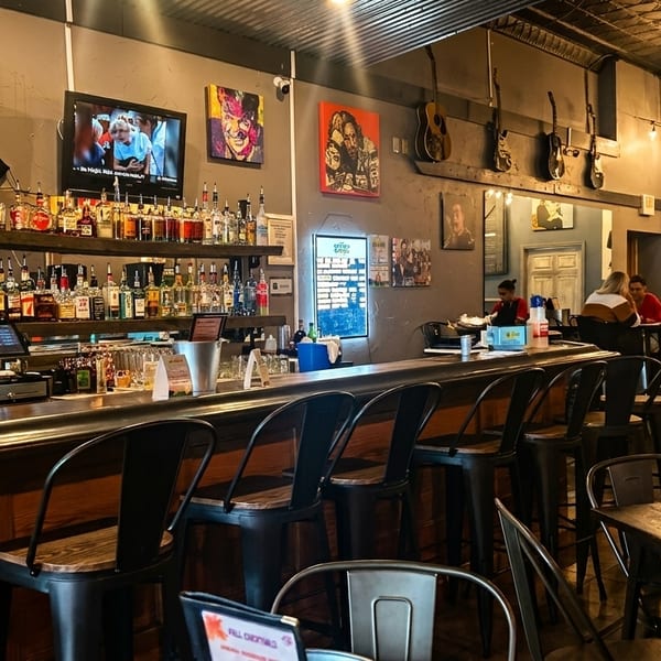 A lively bar area with bottles on shelves, bar stools, TVs, and patrons seated at tables.