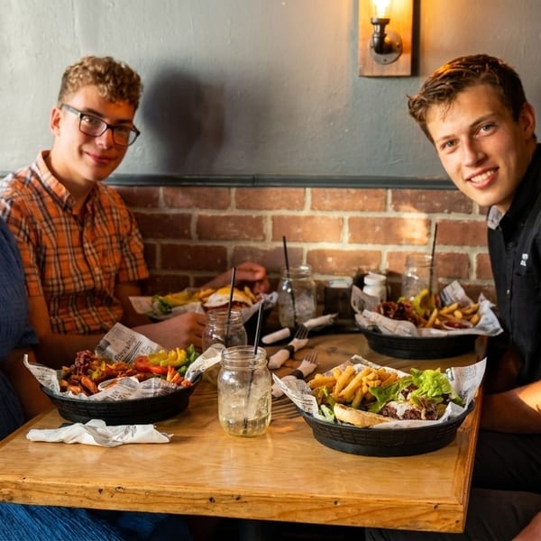 Four smiling people enjoying burgers and fries at a rustic restaurant table.