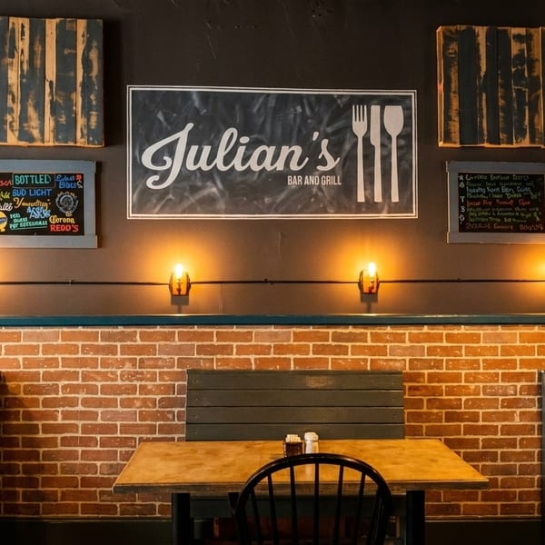 Interior of Julian's Bar and Grill with brick walls, wooden tables, and a sign.