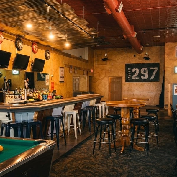 A rustic tavern interior with a long bar, high-top tables, and a pool table.