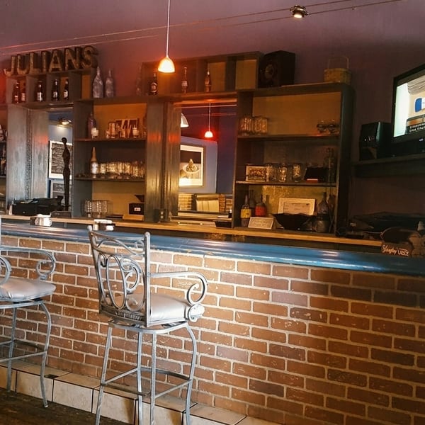 A bar area with a brick facade, bar stools, shelves with bottles and glasses, and a TV.